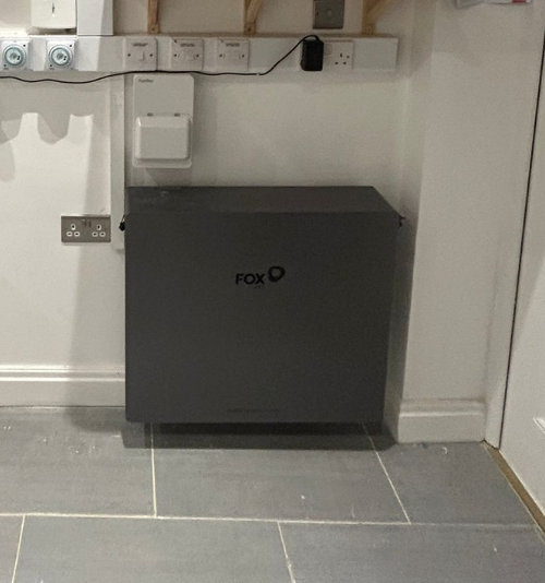 - Flux Solar Energy Gray Fox-branded equipment cabinet against a wall in a utility room, with outlets and cables above it.