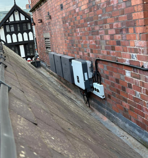- Flux Solar Energy Rooftop scene with brick exterior wall and a row of electrical panels and conduits mounted to the wall, sloped roof in the foreground.